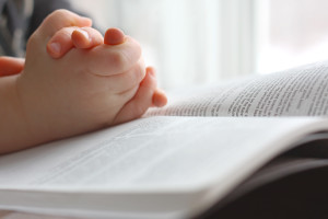 the hands of a young Christian child are folded in prayer over the book the Holy Bible